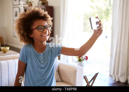 Pre-teen ragazza tenendo un selfie foto in piedi nel soggiorno a ridere, chiudere, il focus sul primo piano Foto Stock