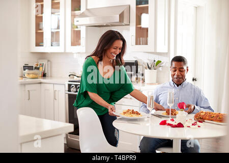 Persone di mezza età razza mista donna donna che serve il suo partner un pasto romantico nella loro cucina, il fuoco selettivo Foto Stock