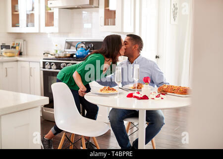 Persone di mezza età razza mista donna donna baciare il suo partner dopo aver servito per lui un pasto romantico nella loro cucina, il fuoco selettivo Foto Stock