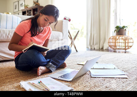 Ragazza adolescente facendo il suo dovere seduto sul pavimento nel soggiorno, angolo basso, close up Foto Stock