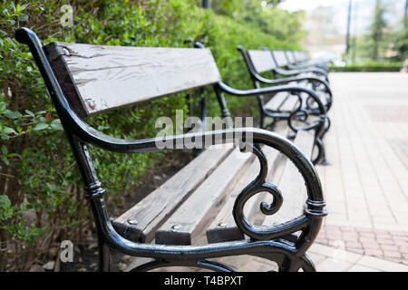 Una fila di legno e metallo panchine lungo un marciapiede in un parco Foto Stock