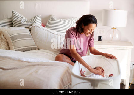 La millenaria razza mista madre seduta sul suo letto la sua consolante Gridando bambino giacente posto letto lei nella sua culla Foto Stock