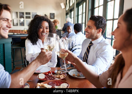 Colleghi di lavoro rendendo Toast seduti a tavola a mangiare pasti Foto Stock