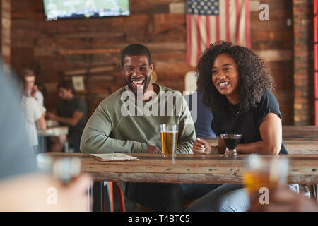Coppia giovane incontro in Sports Bar godendo di bere prima del gioco Foto Stock