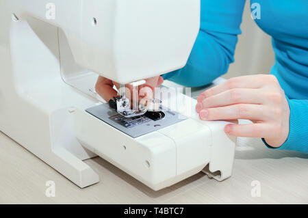 Ragazza caucasica si inserisce una bobina con il filo nella macchina da cucire. Close-up. Foto Stock