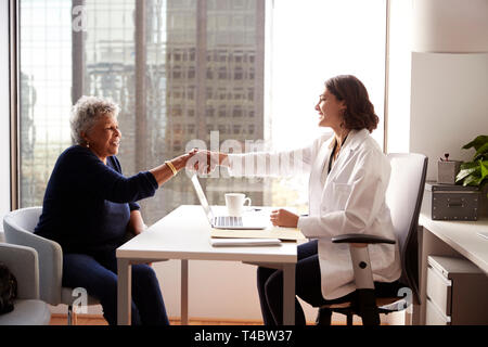 Senior donna stringono le mani con medico donna in ospedale Office Foto Stock