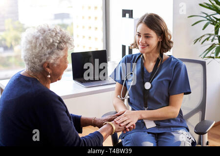 L'infermiera indossando Scrubs In ufficio rassicurante Senior paziente femmina e tenendo le Sue mani Foto Stock