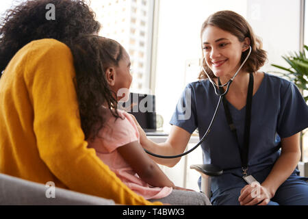 Pediatra femmina indossando Scrubs ascoltando le ragazze il torace con uno stetoscopio in ospedale Office Foto Stock