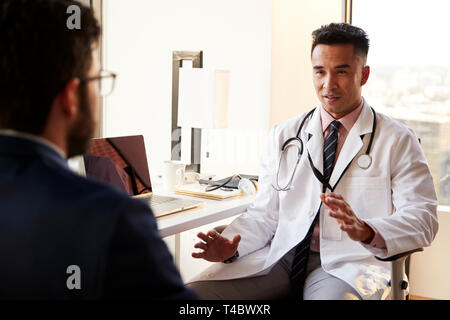 Oltre la spalla dell'uomo avente la consultazione con connettore maschio di tipo medico in ospedale Office Foto Stock