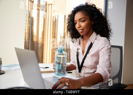 Imprenditrice con Laptop seduto alla scrivania di mantenere idratato bevendo acqua in bottiglia in Office Foto Stock
