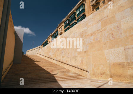 Moderno e lungo le scale di pietra gialla vicino a La Valletta City Gate di Malta e il cielo blu scuro in background Foto Stock