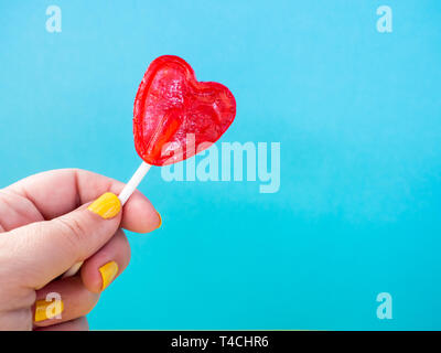 Una donna con verniciato giallo chiodi con un rosso lecca-lecca in mano e sfondo blu Foto Stock