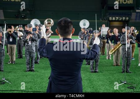 Giappone Aria forza di autodifesa fascia centrale conduttore, il Mag. Satoshi Kuchikata contemporaneamente ripete conducendo la JASDF e USAF membri della band per la cerimonia di apertura della Major League Baseball in Giappone Serie di apertura presso il Tokyo Dome, Marzo 20, 2019. Lo stadio è stato esaurito Foto Stock