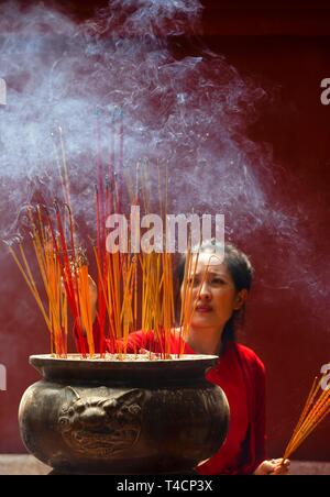 Giovane donna con la masterizzazione di bastoncini di incenso sul nuovo anno cinese, complesso tempio Wat Phnom Penh Daun, Phnom Penh Cambogia Foto Stock