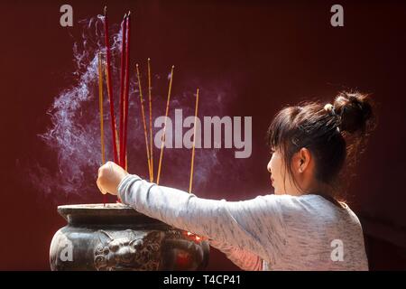 Giovane donna con la masterizzazione di bastoncini di incenso sul nuovo anno cinese, complesso tempio Wat Phnom Penh Daun, Phnom Penh Cambogia Foto Stock