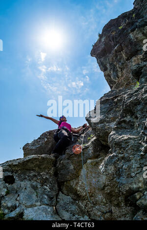 Gioiosa giovane donna agitando la mano in aria dopo il passaggio di un tratto difficile su una via ferrata in Baia de Fier, contea di Gorj, in Romania, su th Foto Stock