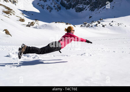 Femmina gioiosa escursionista saltellando sulla neve, orizzontalmente, somigliante ad un Superman/Superwoman pongono la levitazione, vicino Malaiesti hut, Bucegi/moun dei Carpazi Foto Stock