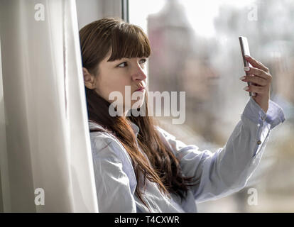 Ragazza giovane rende selfie seduti mediante la finestra Foto Stock