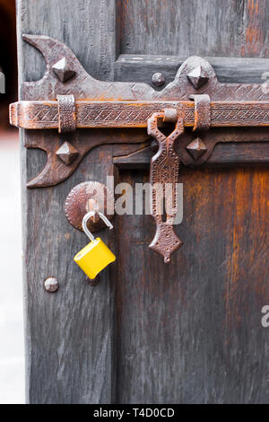 Potente vite forgiato scolpito con ornamenti e parti per la chiusura di una vecchia porta di legno con la formazione di ruggine sul catenaccio e moderno aperto il lucchetto giallo, come un Foto Stock