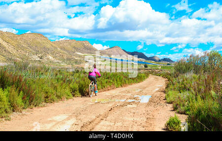La donna in sella ad una mountain bike con un percorso fangoso di sporcizia. Sport sano sul verde del prato che la circonda. Foto Stock