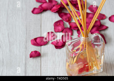 Pettine diffusore di fragranza in un vasetto di vetro con petali di rosa su un grigio Sfondo di legno Foto Stock