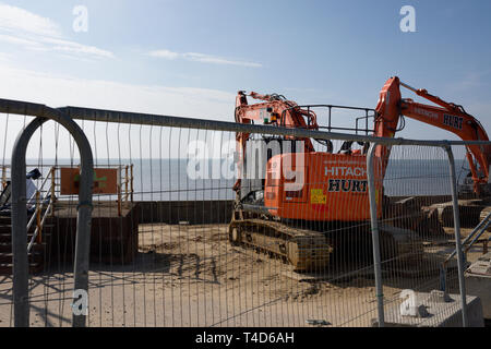 Due escavatori idraulici arancioni dietro la recinzione di sicurezza sulle difese marine di Anchorsholme a blackpool, lancashire, regno unito Foto Stock