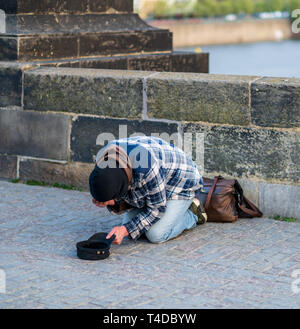 Il freddo senzatetto sulle ginocchia per l'accattonaggio denaro da turisti sul Ponte Carlo a Praga - Primavera 2019 Foto Stock