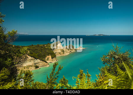 Cape Drastis (Perulades) con acque blu cristallo del mare su una soleggiata giornata estiva con foglie in primo piano (Corfu, Grecia, Europa) Foto Stock