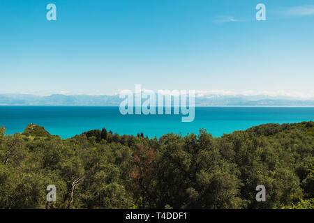 Vista da cape Drastis (Perulades) verso l'Albania e le sue montagne con acque blu cristallo del mare su una soleggiata giornata estiva (Corfù, Grecia, Europa) Foto Stock