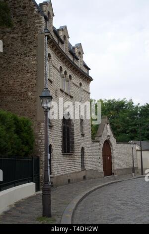 Montmart angolo di strada - edificio tradizionale in pietra, alte siepi verdi, strada di ciottoli e pavimentazione con cordolo, lampost alti in primo piano, muro di pietra Foto Stock