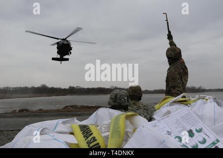 Il Nebraska Esercito Nazionale soldati di guardia, PFC. Kyle giovani (a destra), SPC. Rasmussen (centrale) e PFC. Giacobbe McCarthy (sinistra) attendono un inbound UH-60 Blackhawk elicottero durante le operazioni di sandbagging vicino a Genova, Nebraska Marzo 23. Il Nebraska esercito nazionale Guard elicottero e gli equipaggi di terra sono state conducendo contrappeso air drop missioni a sostegno del 2019 inondazioni. (Nebraska Guardia Nazionale Foto Stock