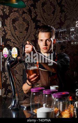 Grodno, Bielorussia - Maggio 02, 2017: elegante il barista si versa la birra nel bicchiere da birra tocca nella barra di Londra Foto Stock