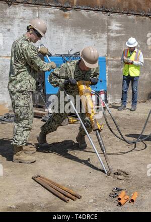 OXNARD in California (Mar. 20, 2019) - USA Navy Builder 2a classe Brock agricoltore (sinistra) da Arlington, Texas, e costruzione meccanico 2a classe Graham Milstead, da Eagle, Idaho, entrambi assegnati alla costruzione subacquea Team 2, jackhammer un ancoraggio nel terreno per fornire supporto alla banchina expeditionary patch a parete (Curley patch) durante una prova di concetto il test a bordo della base navale di Ventura County a sostegno del Pacifico Blitz 2019 (PacBlitz19). La patch Curley tecnica fornisce conveniente riparare ai moli e banchine di abilitazione delle forze militari di continuare ad utilizzare la porta per fornire supporto logistico Foto Stock