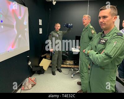 Royal Air Force Flight Lt. Darren francese, formazione pilota Avanti 2.0 istruttore pilota e la RAF senior rappresentante nazionale mette in evidenza di realtà virtuale le funzionalità auricolare a British Army Col. Paddy Logan (centro), Assistente direttore per la formazione di volo per RAF sede 22 del gruppo e RAF Squadron Leader Steve Smith (sinistra) presso il PTN struttura presso le Forze Armate di riserva nel centro di Austin, Texas, Marzo 18, 2019. La RAF hanno entrambi uno studente-pilota e un istruttore pilota che partecipano alla classe come essi guardano a introdurre il PTN lezioni apprese nella loro formazione di volo pipeline. Foto Stock