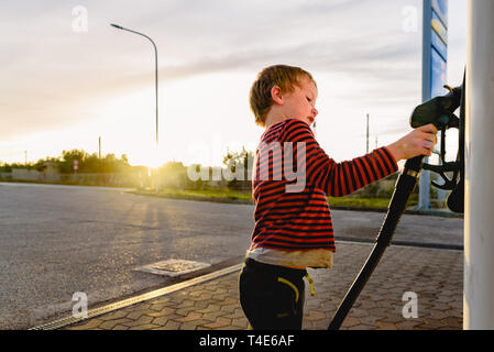 Bambino tenere il tubo di una pompa del carburante al tramonto in corrispondenza di una stazione di gas. Foto Stock
