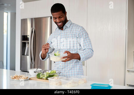 Uomo in cucina la preparazione di alta farina proteica e la messa di porzioni in contenitori in plastica Foto Stock