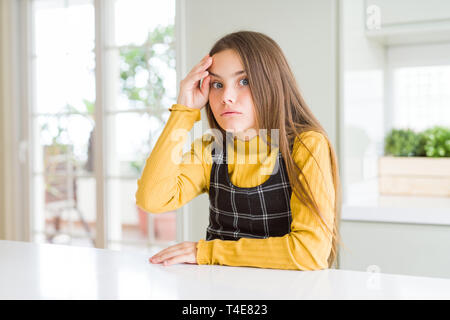 Giovane bella bionda kid bambina indossa casual maglione giallo a casa preoccupata e sottolineato circa un problema con la mano sulla fronte, nervosi e ansiosi Foto Stock