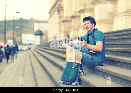 Sorridente uomo caucasico utilizzando il telefono cellulare mentre è seduto sui gradini - happy tourist cercando le indicazioni della mappa sullo smartphone - traveler con zaino Foto Stock