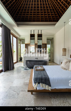 Un ambiente accogliente e lussuoso letto in una villa con bella casa interno in Kuta sull'Isola di Lombok, Indonesia e una vasca da bagno realizzata in pietra Foto Stock