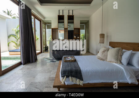 Un ambiente accogliente e lussuoso letto in una villa con bella casa interno in Kuta sull'Isola di Lombok, Indonesia e una vasca da bagno realizzata in pietra Foto Stock