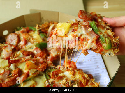 Raccolta a mano una fetta di stretching Cheesy Pizza dalla scatola Foto Stock