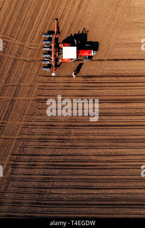 Vista aerea di agricoltore e il trattore con raccolto una seminatrice montata durante la semina del mais in campo, vista dall'alto Foto Stock