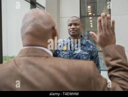 Master-at-Arms di terza classe Desravines Rodelin, un membro del supporto navale attività Bethesda le forze di sicurezza, è reenlisted da Barry Bradwell, la NSA Bethesda le forze di sicurezza direttore, nel Bldg. 17 atrium Aprile 5, 2019. Foto Stock