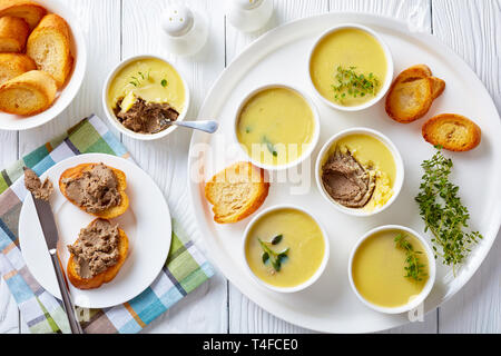 In casa il patè di fegato con erbe aromatiche e burro in ramekins su un piatto di portata con le fette biscottate di baguette e pate fegato panini su di una piastra orizzontale di vi Foto Stock