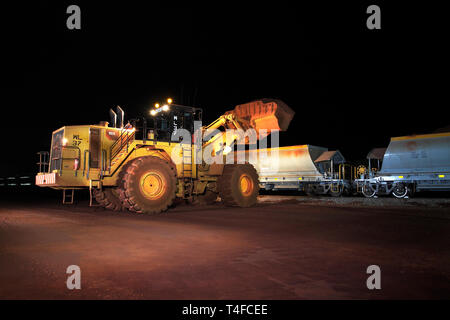 Testa di rampa operazioni alla miniera con i carri nuovi sul treno essendo caricato con ematite il minerale di ferro di stock di notte prima di recarsi alla porta per la vendita all'estero Foto Stock