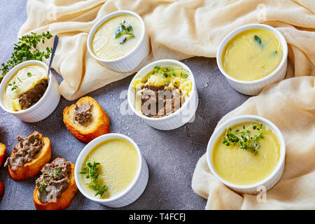 In casa di velluto di seta liscia di fegato di pollo pate con erbe aromatiche, cognac e burro in ramekins su un tavolo in cemento con fette biscottate di baguette, francese Foto Stock