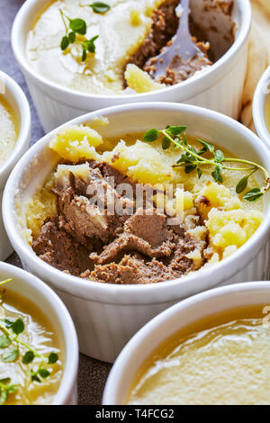 Close-up di velluto di seta liscia di fegato di pollo pate con erbe aromatiche, cognac e burro in ramekins su un tavolo in cemento con fette biscottate di baguette, fren Foto Stock