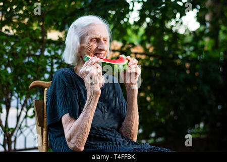 Allegro nonna mangiare anguria nel cortile posteriore Foto Stock