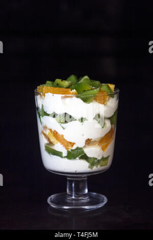 Il dessert stratificata in vetro trasparente, yogurt, arancio, kiwi, i dadi su uno sfondo scuro. Il concetto di sana e corretta e semplice cibo sano Foto Stock