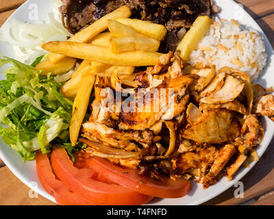 Döner Kebab sul piatto con patatine fritte, pomodori, riso, cipolla e insalata. Pollo alla griglia e carne di agnello con verdure. Foto Stock
